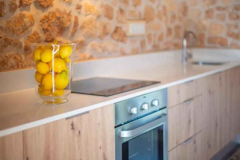 A kitchen with a cooktop, oven, and a glass of lemons on the counter.