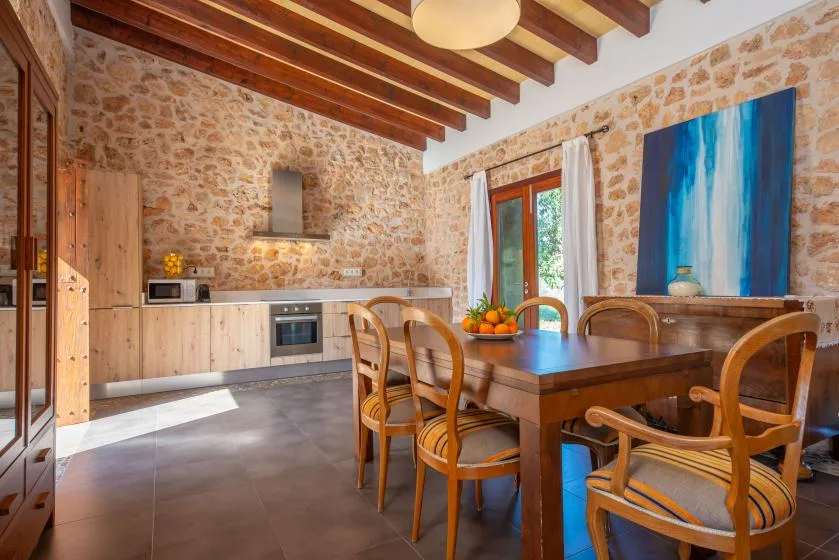 A rustic kitchen and dining area with a wooden table and stone walls.