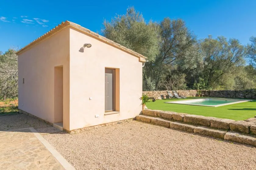 A small stucco outbuilding beside a lawn and swimming pool.