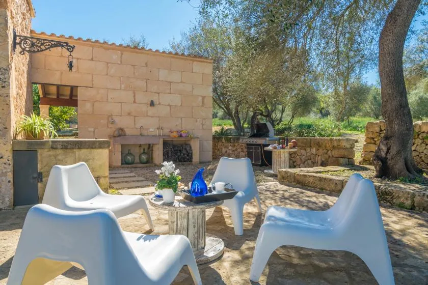 An outdoor stone patio with white seating and a leafy tree.