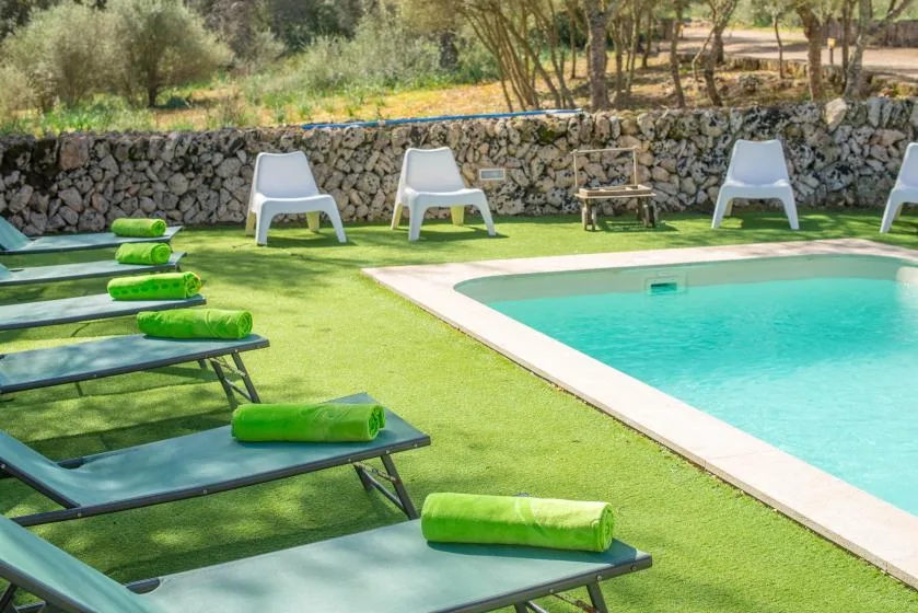An outdoor swimming pool bordered by loungers and a stone wall.
