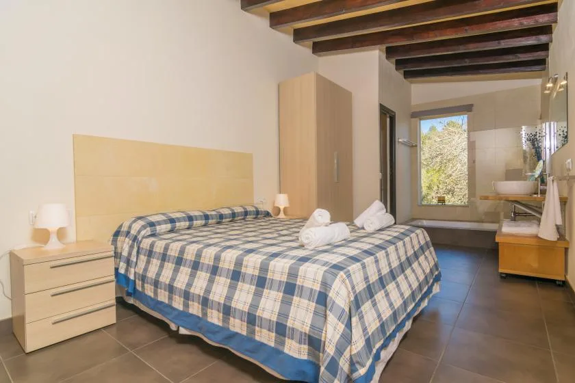 A bedroom with a plaid bedspread and an open bathroom area.