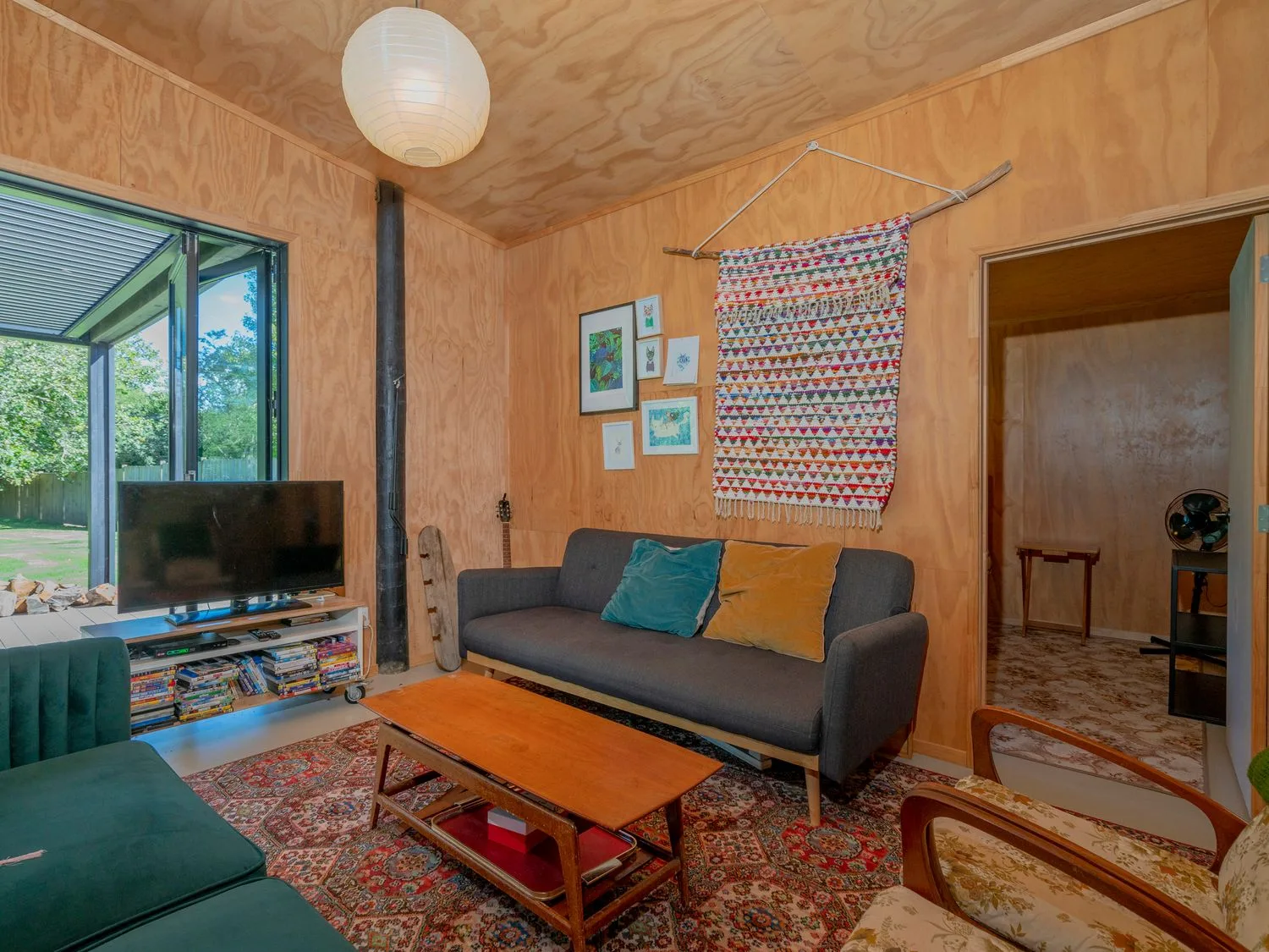 Una sala con un sofá oscuro, una mesa de centro de madera, un televisor y una alfombra estampada en The Pumpkin Shed Kuaotunu Holiday Home, en Kuaotunu