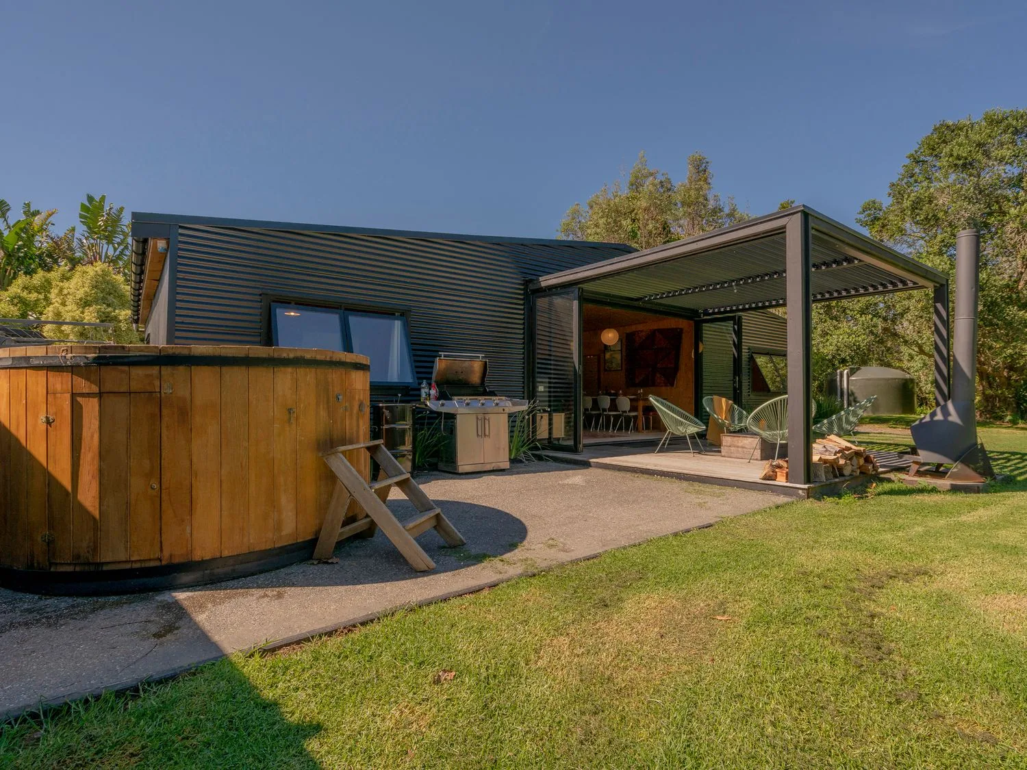 Un patio exterior con una zona de estar cubierta y una bañera de hidromasaje de madera.