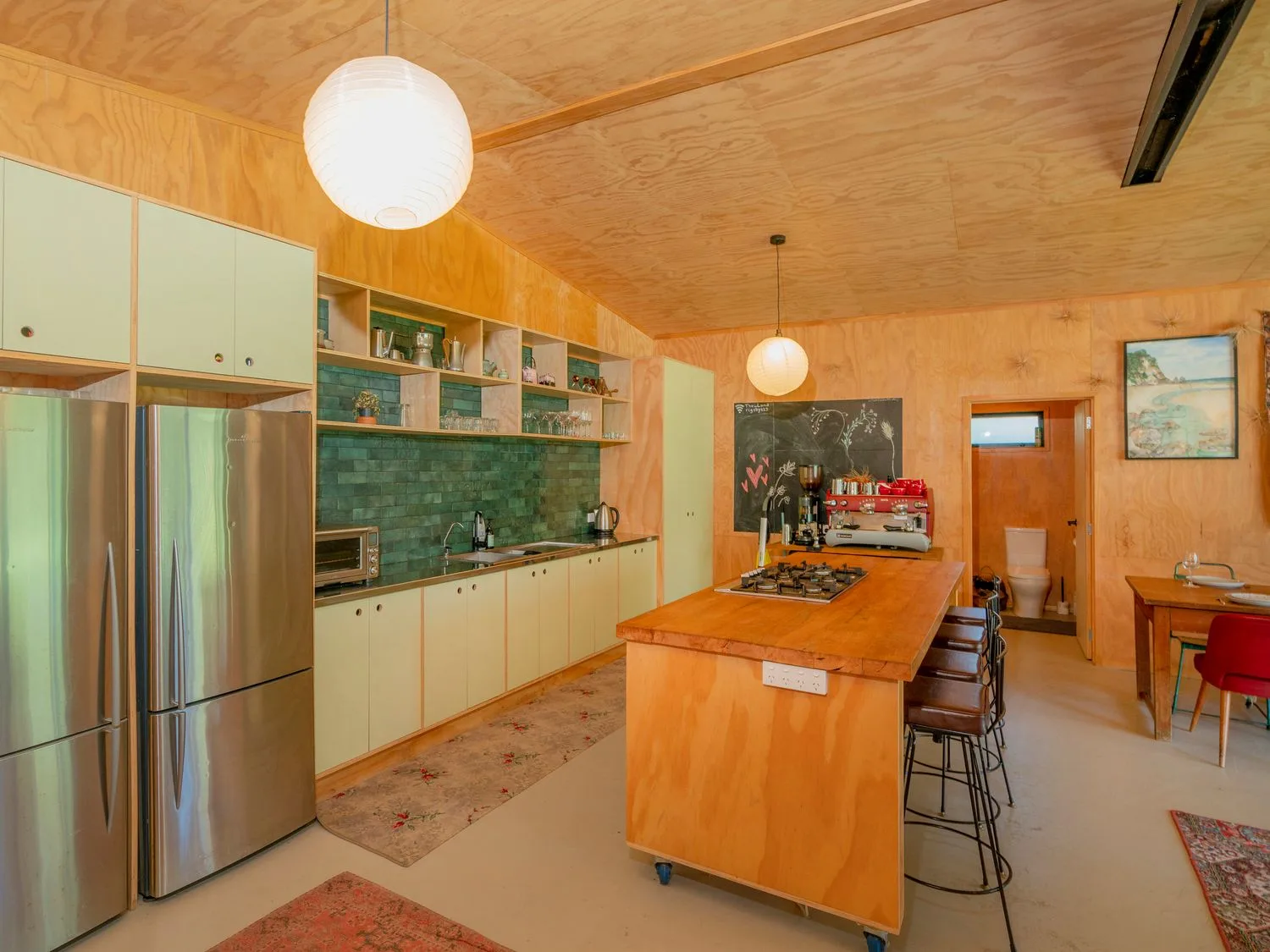 Una cocina con una isla de madera, refrigeradores de acero inoxidable y un salpicadero de azulejos verdes.