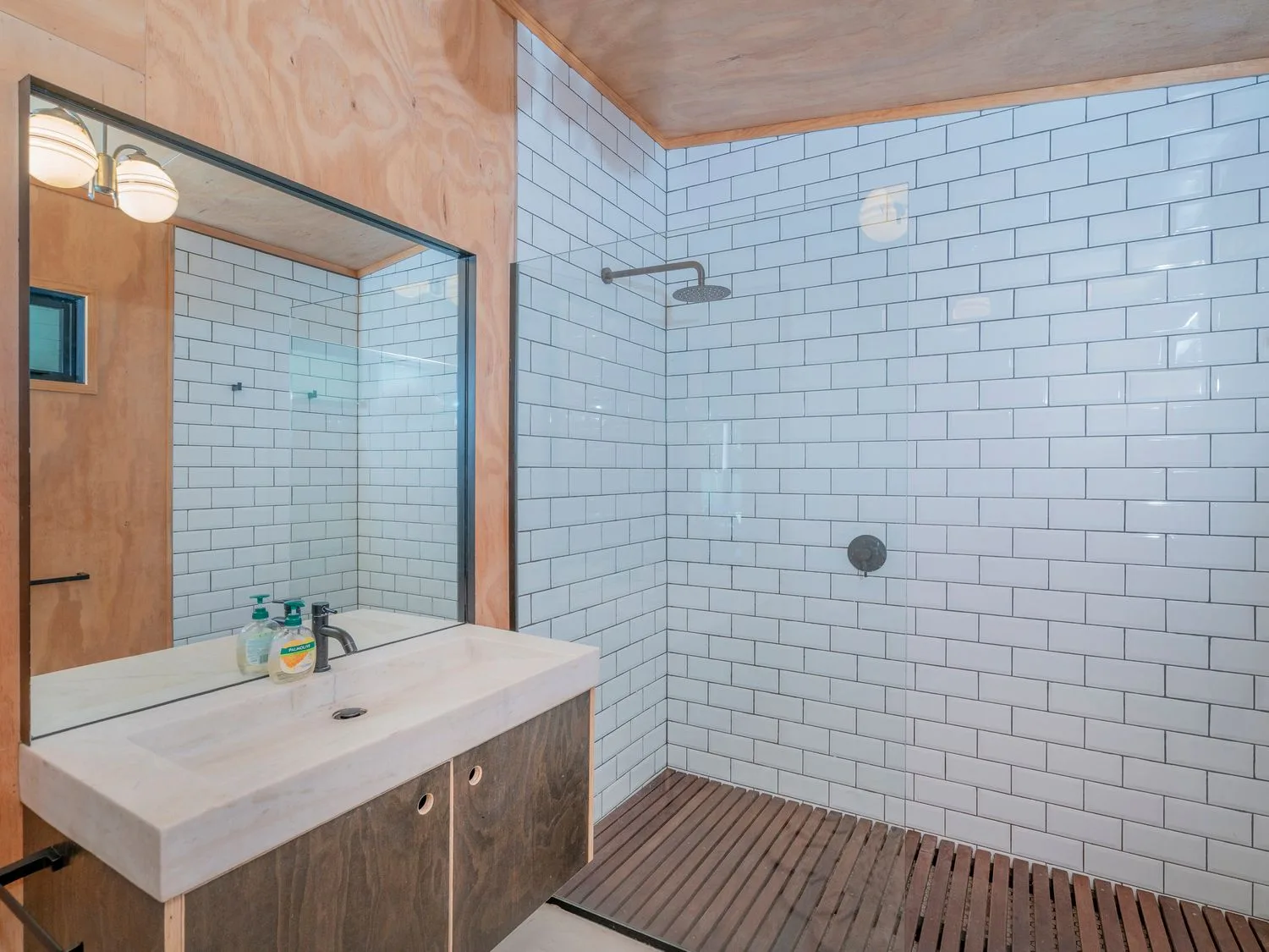 Un baño con lavabo, espejo, ducha con azulejos y suelo de listones.