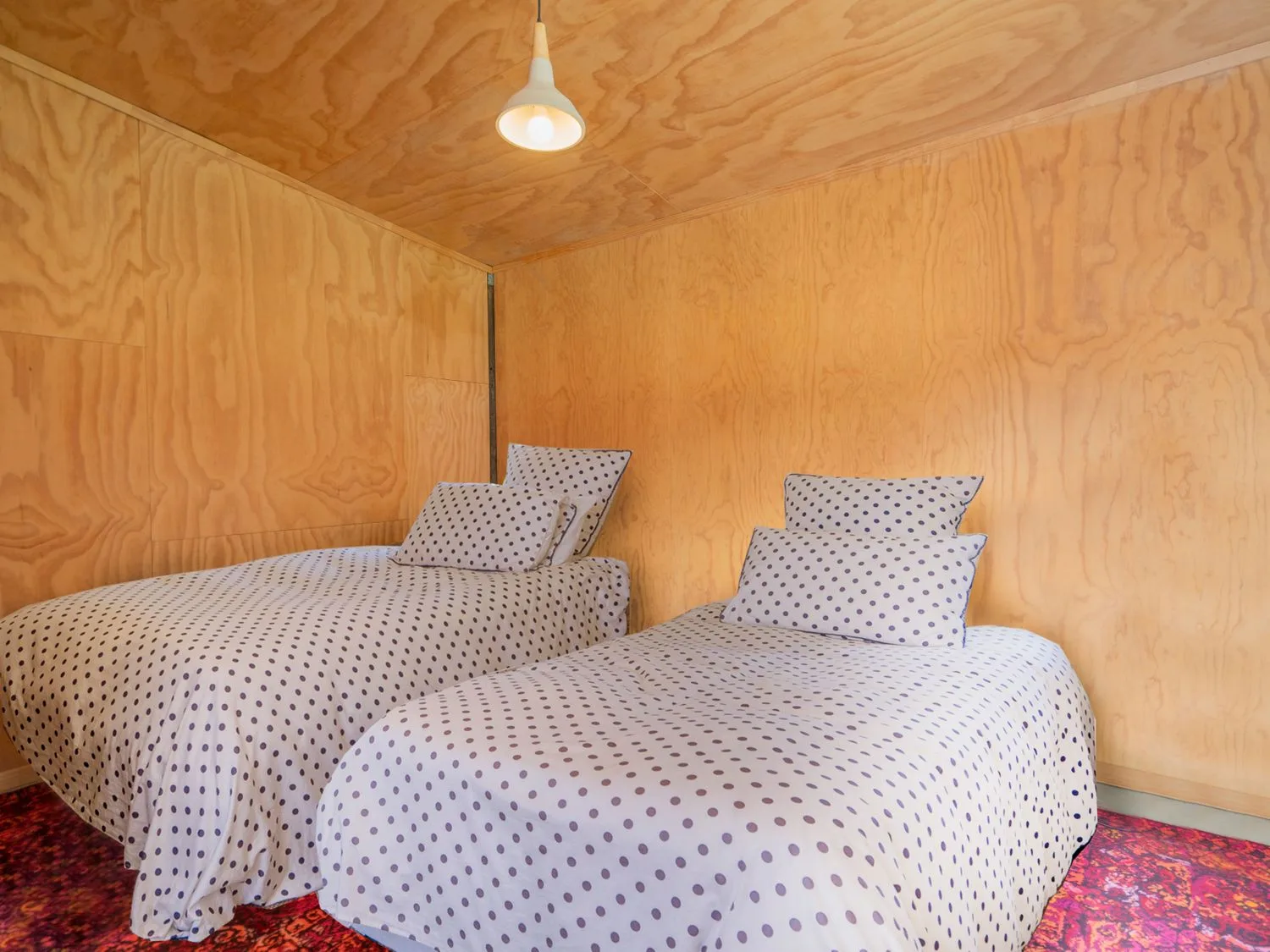 Un dormitorio con dos camas individuales con ropa de cama de lunares y paredes de madera en The Pumpkin Shed Kuaotunu Holiday Home, en Kuaotunu