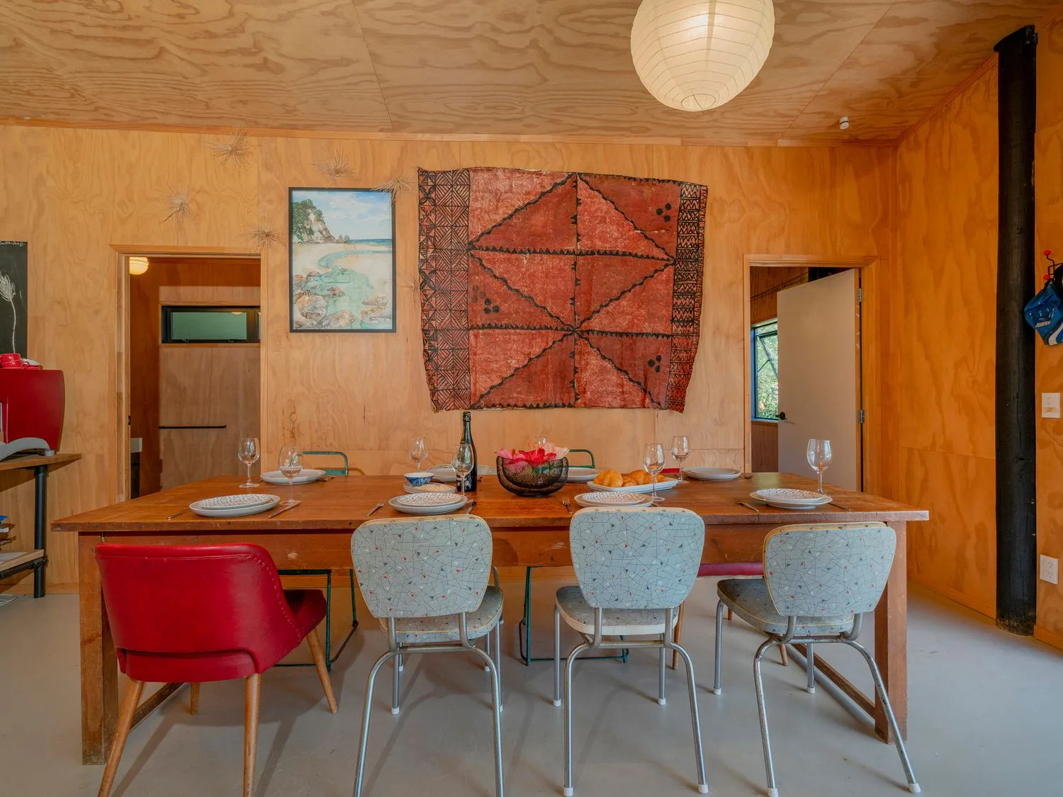 Un comedor con una mesa larga, varias sillas y un tapiz estampado en la pared.
