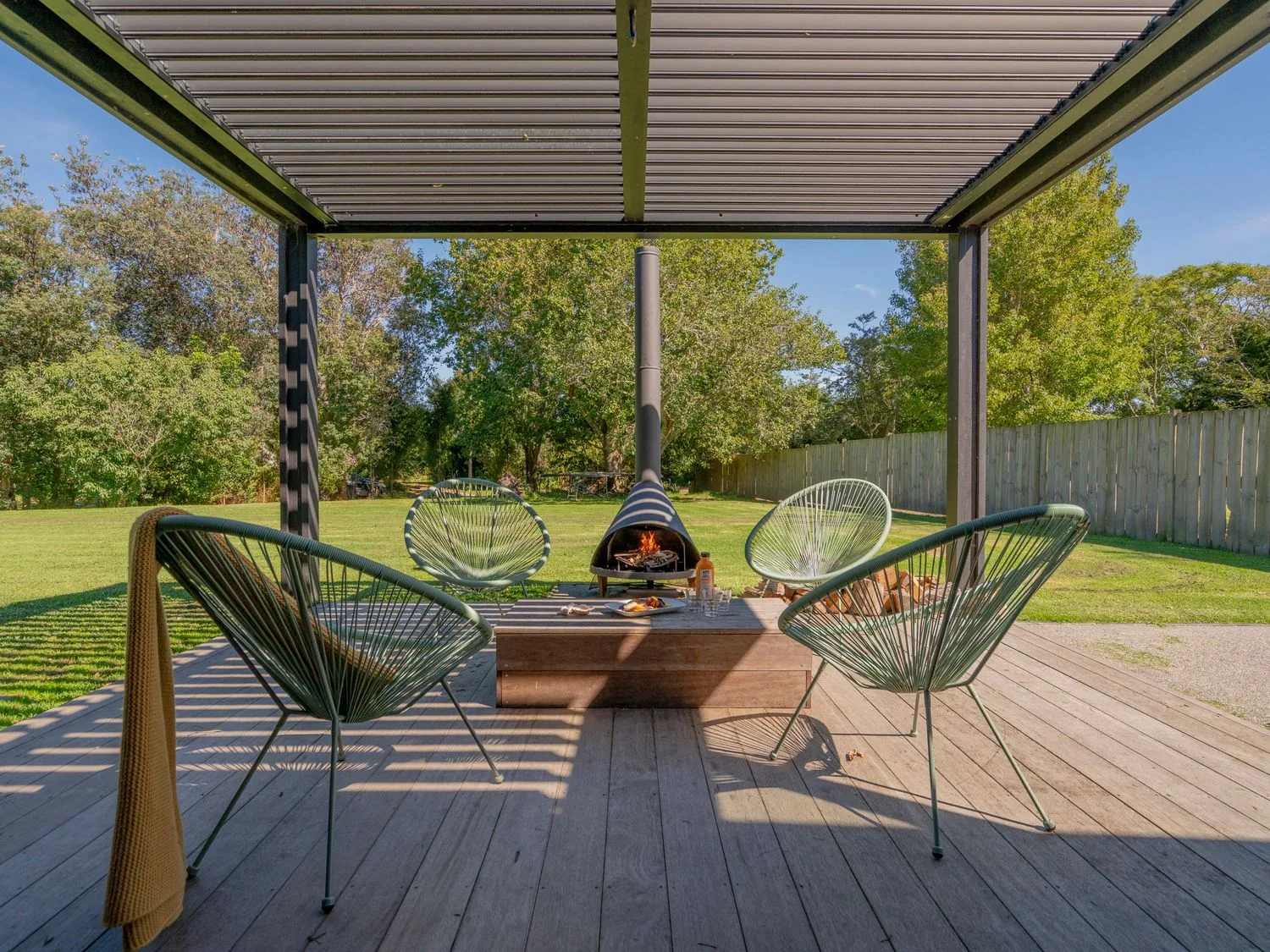 Un patio exterior cubierto con asientos alrededor de una mesa baja y un brasero encendido.