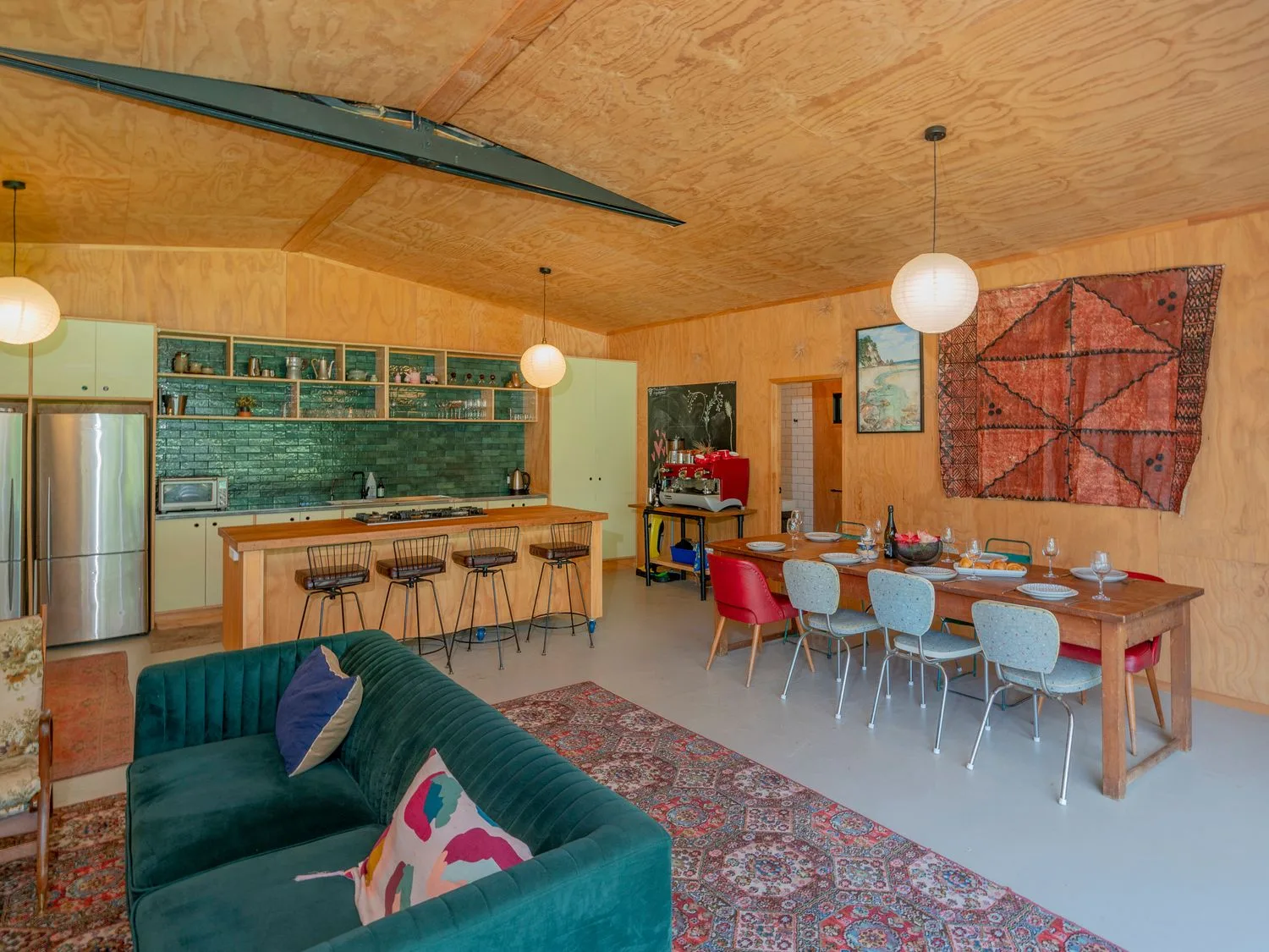 Una cocina y un comedor con paredes y techo de madera, un sofá verde y una mesa de comedor de madera con sillas en The Pumpkin Shed - Kuaotunu Holiday Home, en Kuaotunu