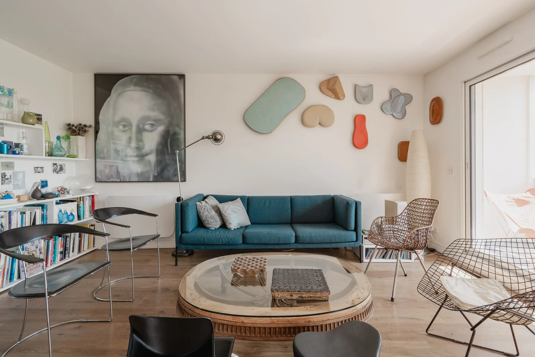 A living room with teal seating, a glass-topped coffee table, and colorful wall art.