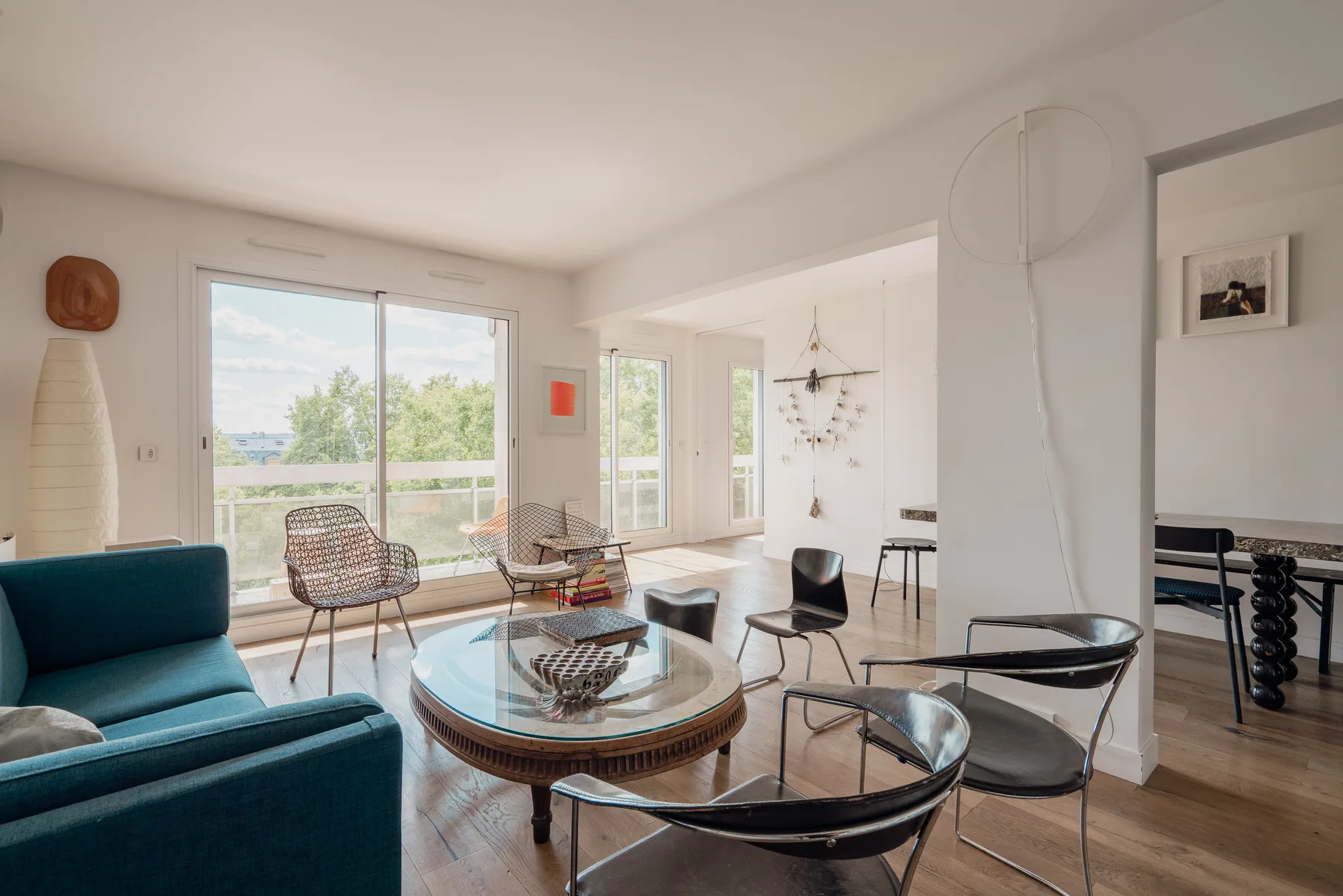 A bright living room with glass doors opening onto a balcony and several seating areas.
