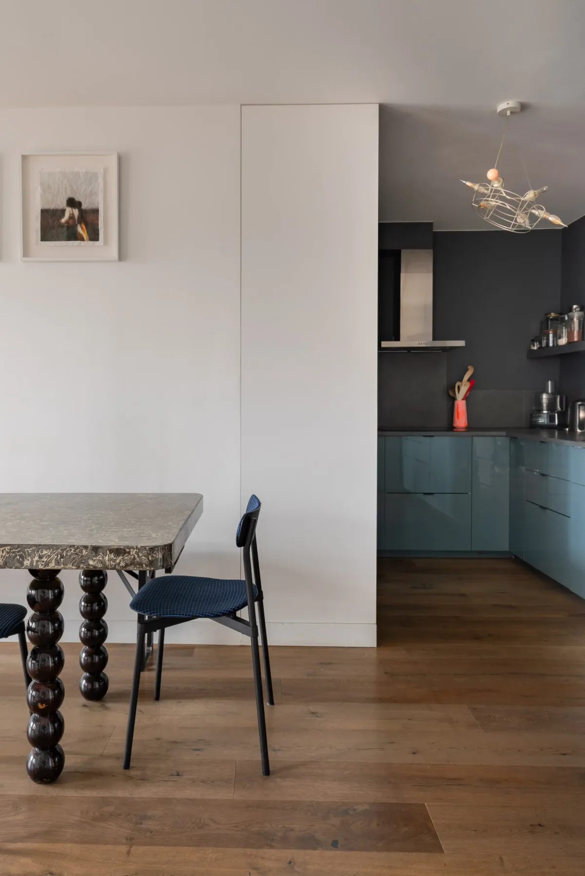 A dining area opens onto a kitchen with teal cabinets.