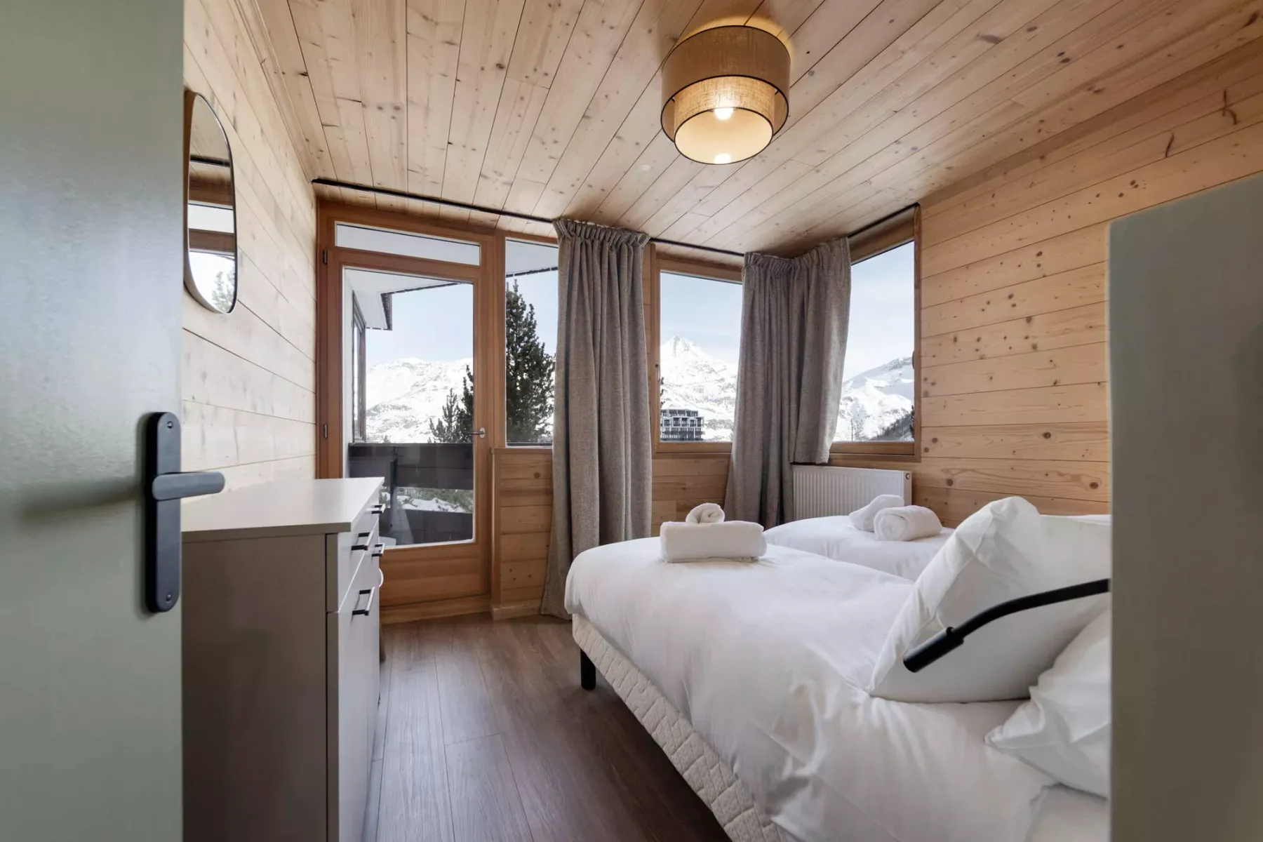 Un dormitorio revestido de madera, con ropa de cama blanca y ventanas con vistas a un paisaje nevado.