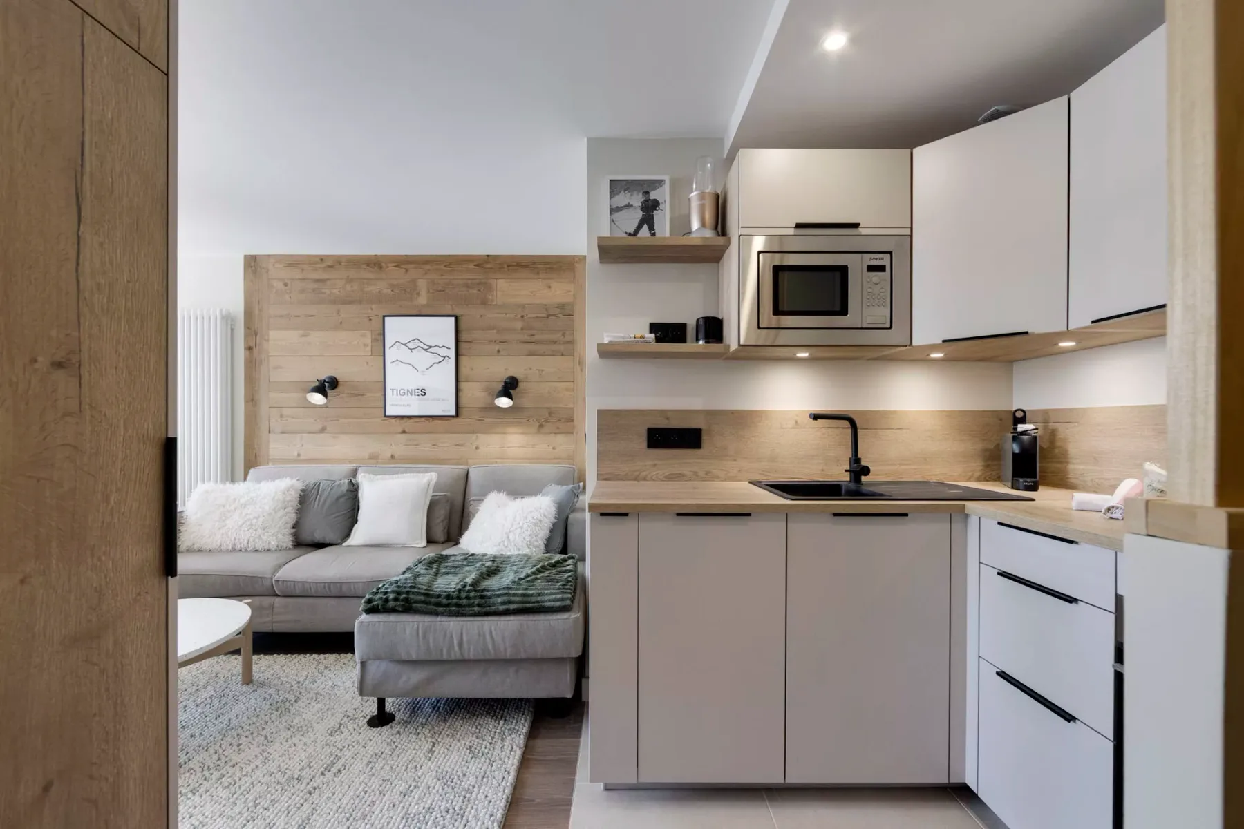 A compact open-plan kitchen and living area with light cabinetry and a gray seating area.