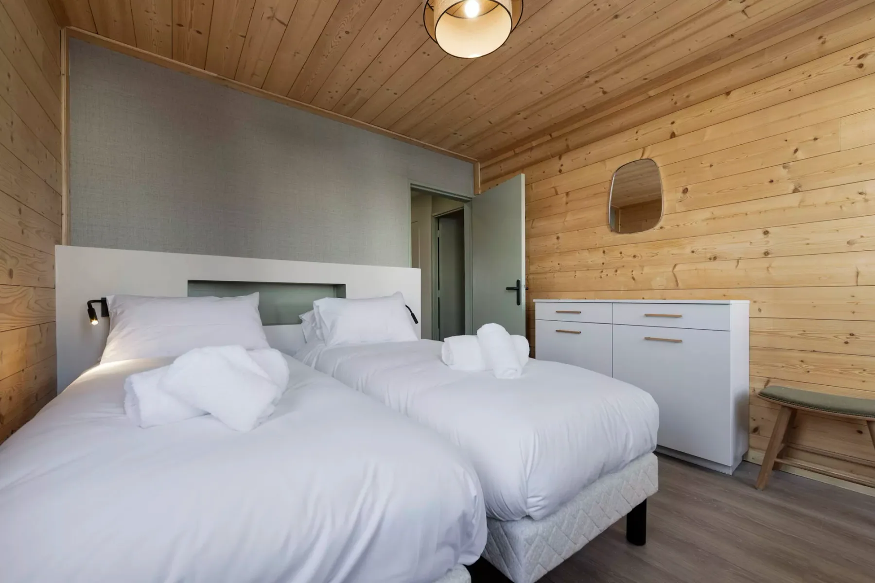 Un dormitorio con dos camas, ropa de cama blanca y paredes revestidas de madera clara.