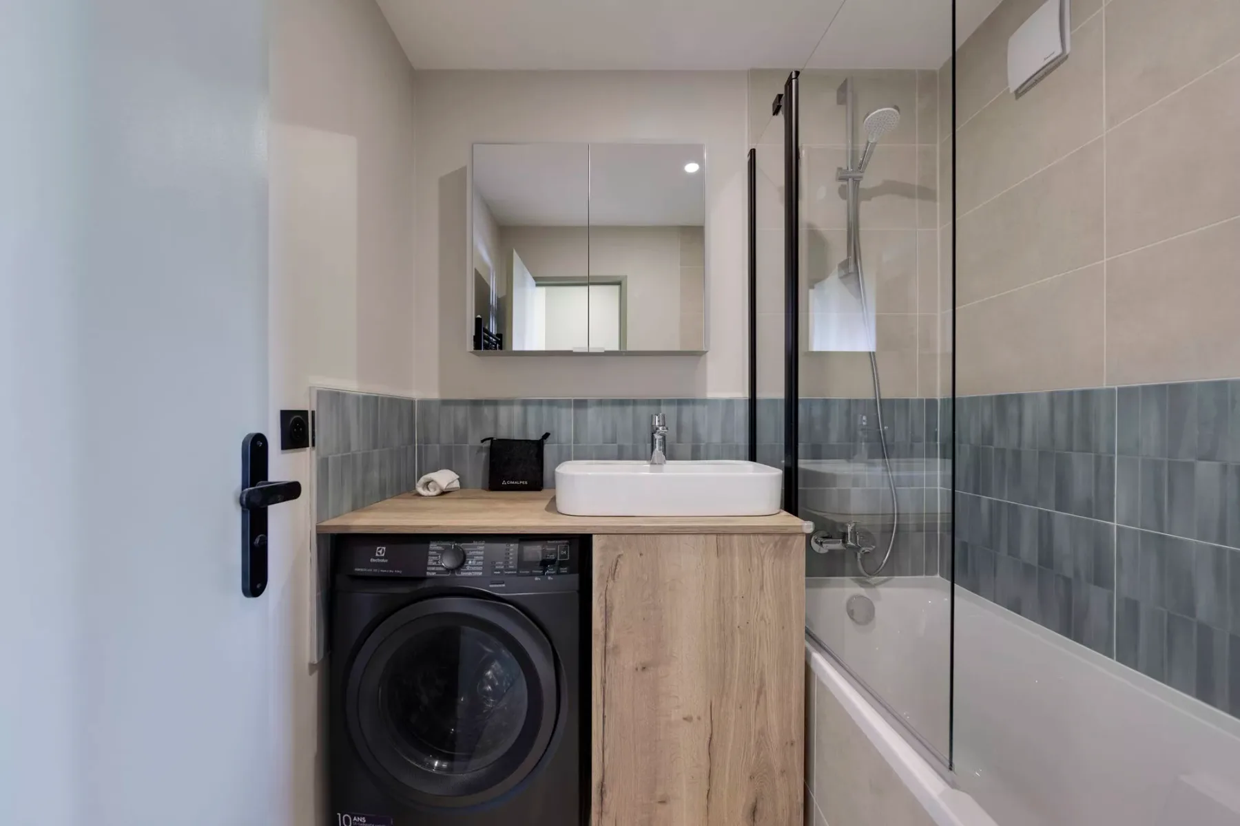 Un baño con lavabo, lavadora y mampara de ducha de vidrio.