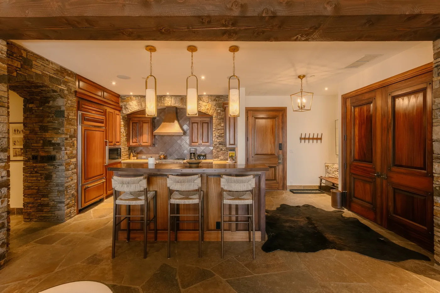 A warm-toned kitchen with a central island, pendant lights, and dark wood cabinetry.