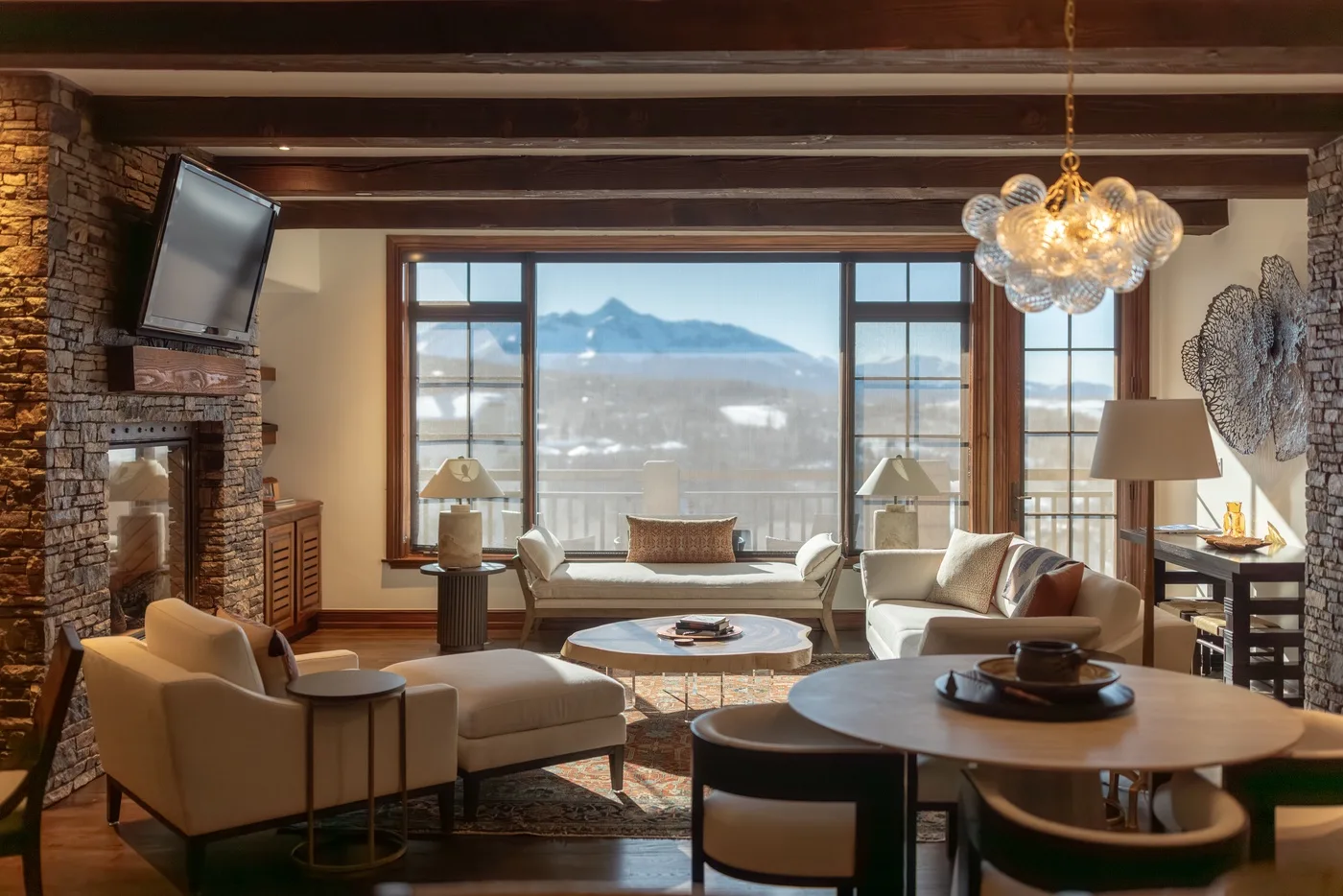 A living room with seating arranged around tables and a wide window overlooking mountains.