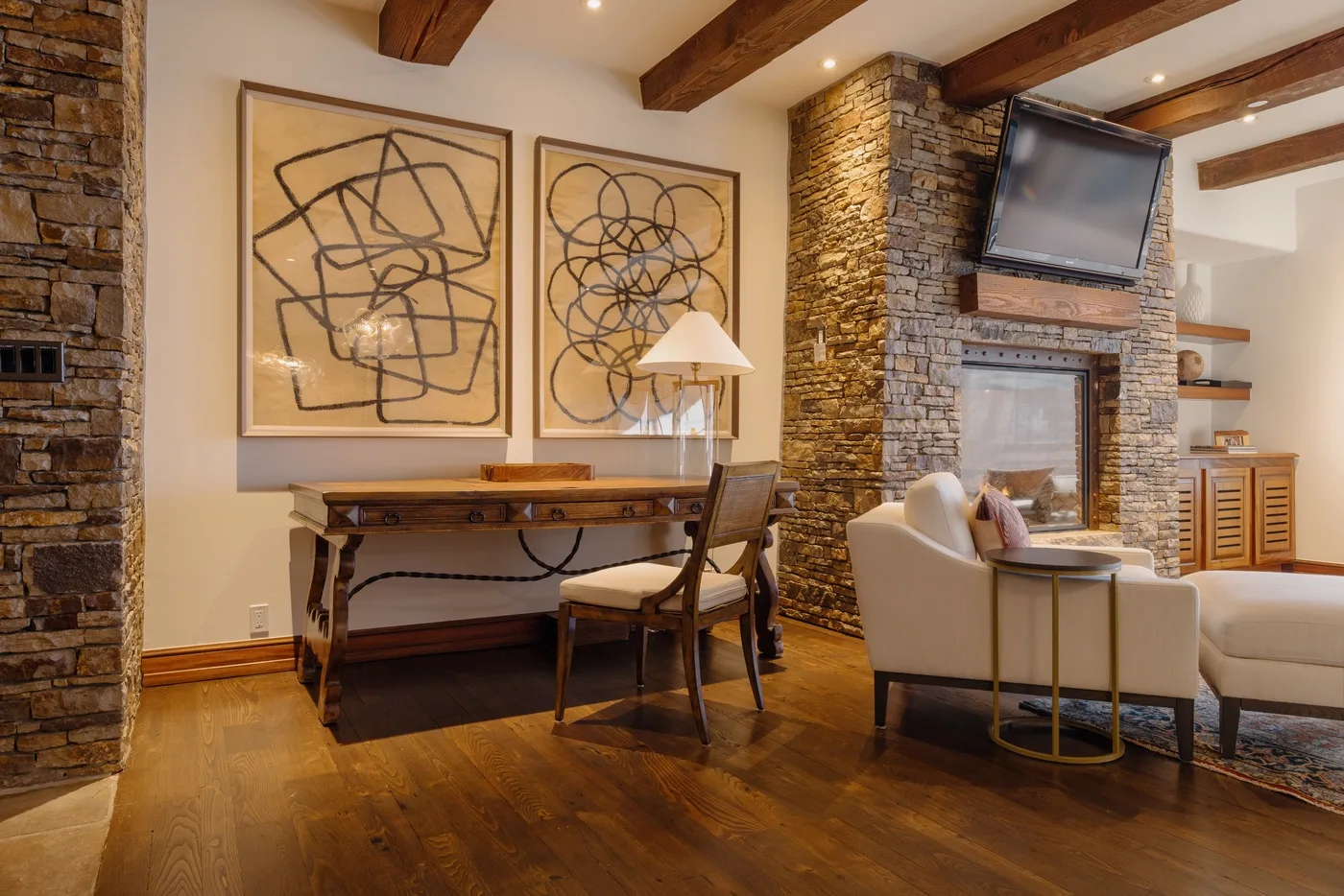 A living room with a desk and seating beside a stone fireplace.