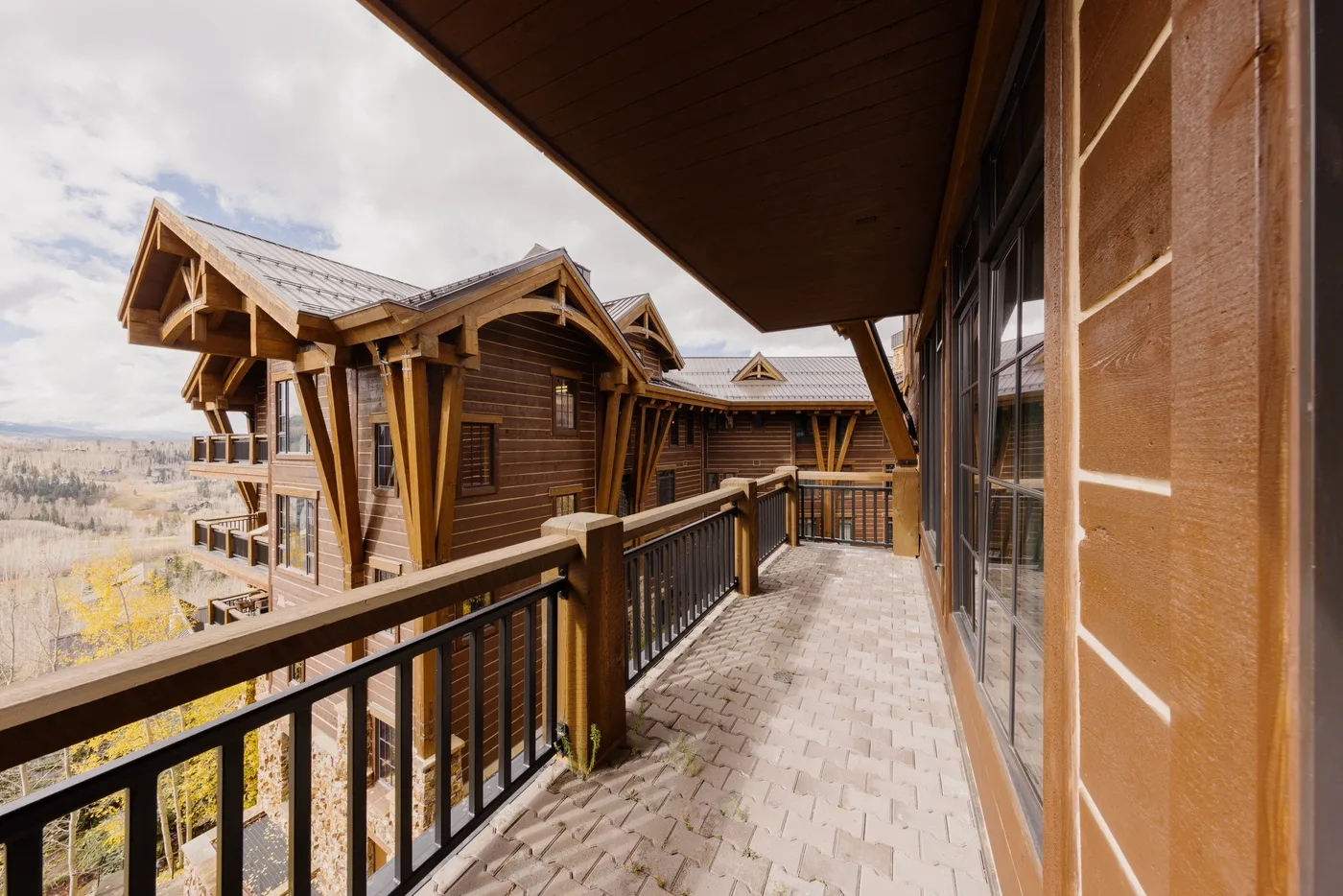 A covered outdoor walkway runs beside a wooden building, with a railing overlooking the landscape.