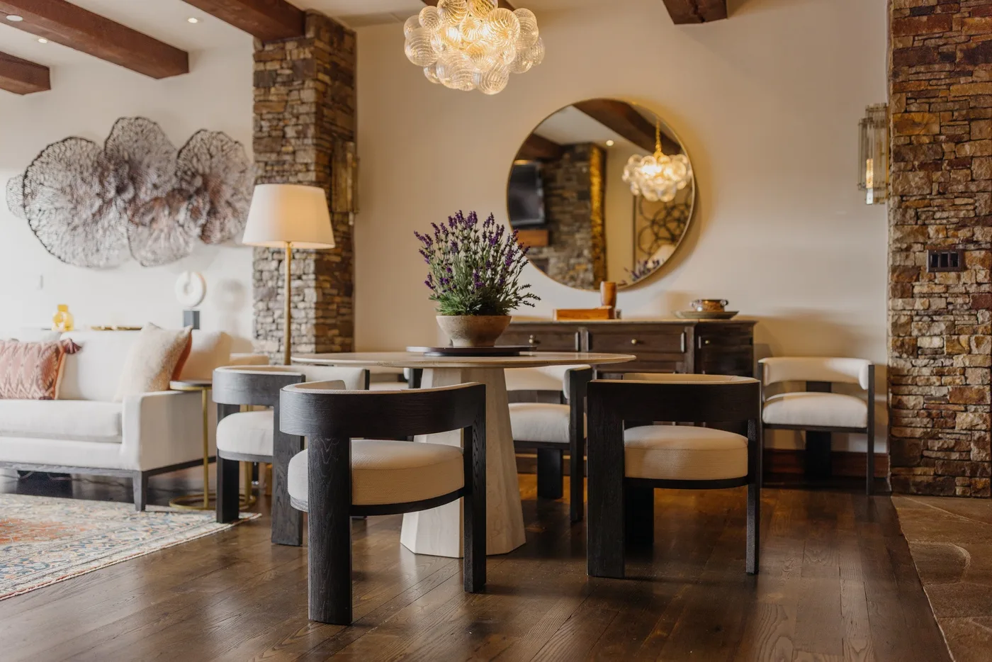 A dining area with a dark table, upholstered chairs, and a round mirror.