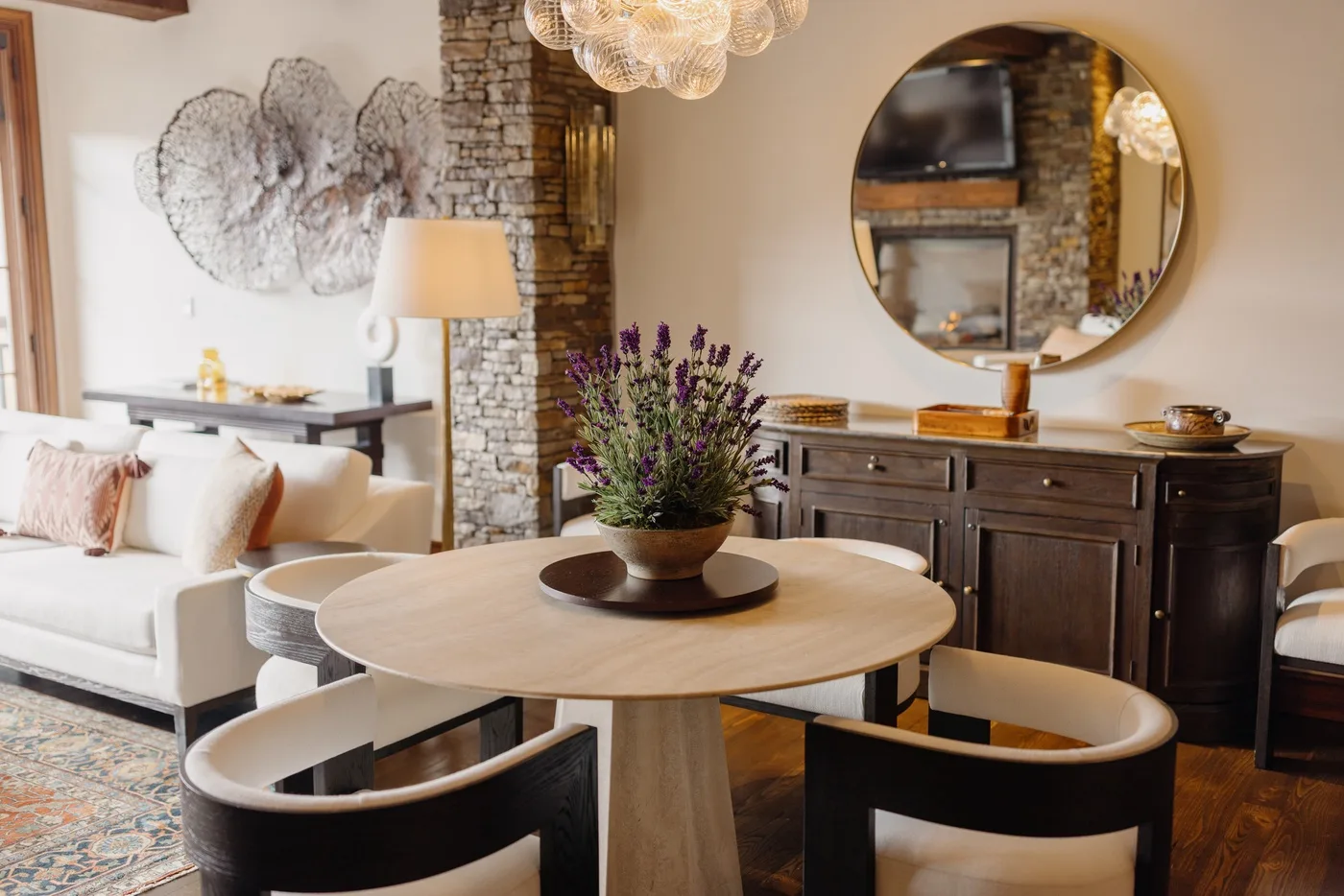 A dining area with a round table, dark chairs, and a large wall mirror.