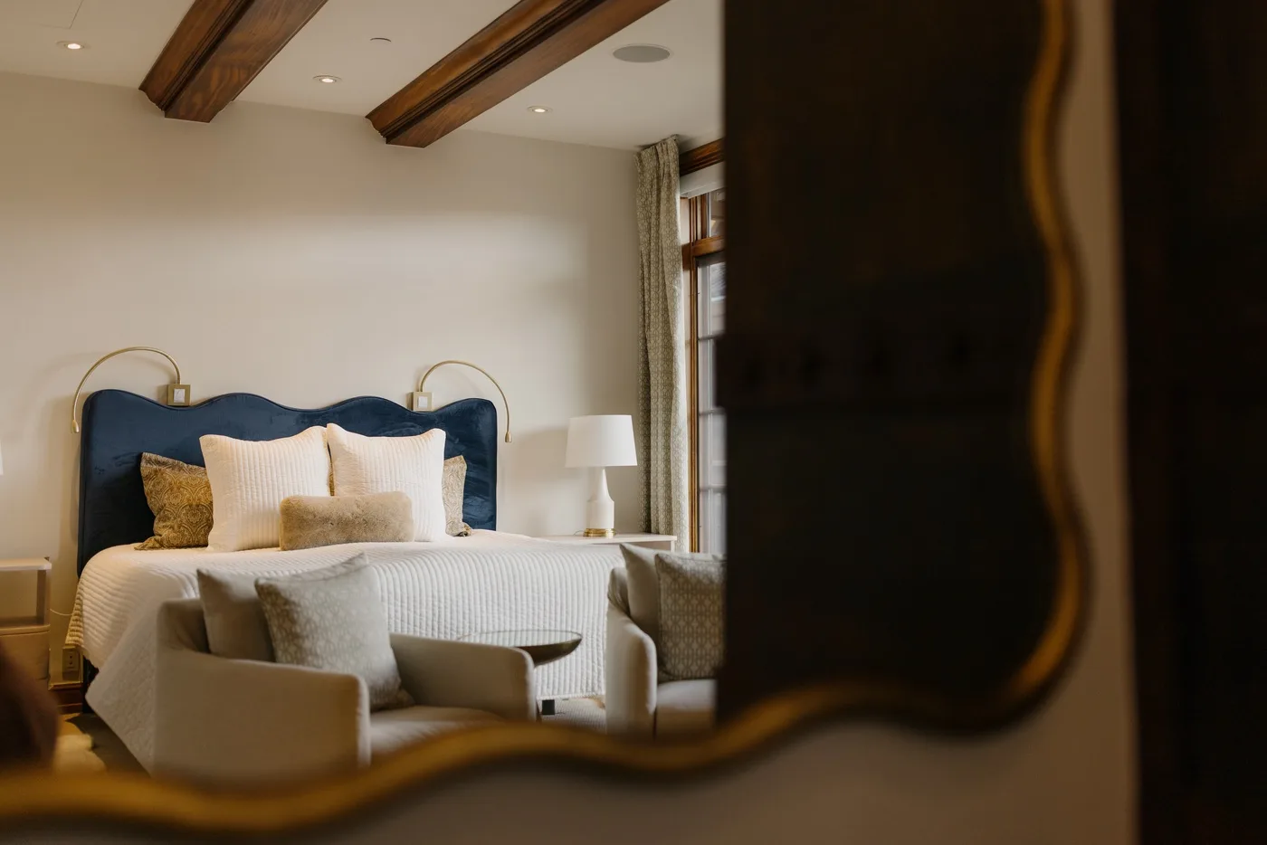 A bedroom with a bed, upholstered seating, and exposed wooden ceiling beams.