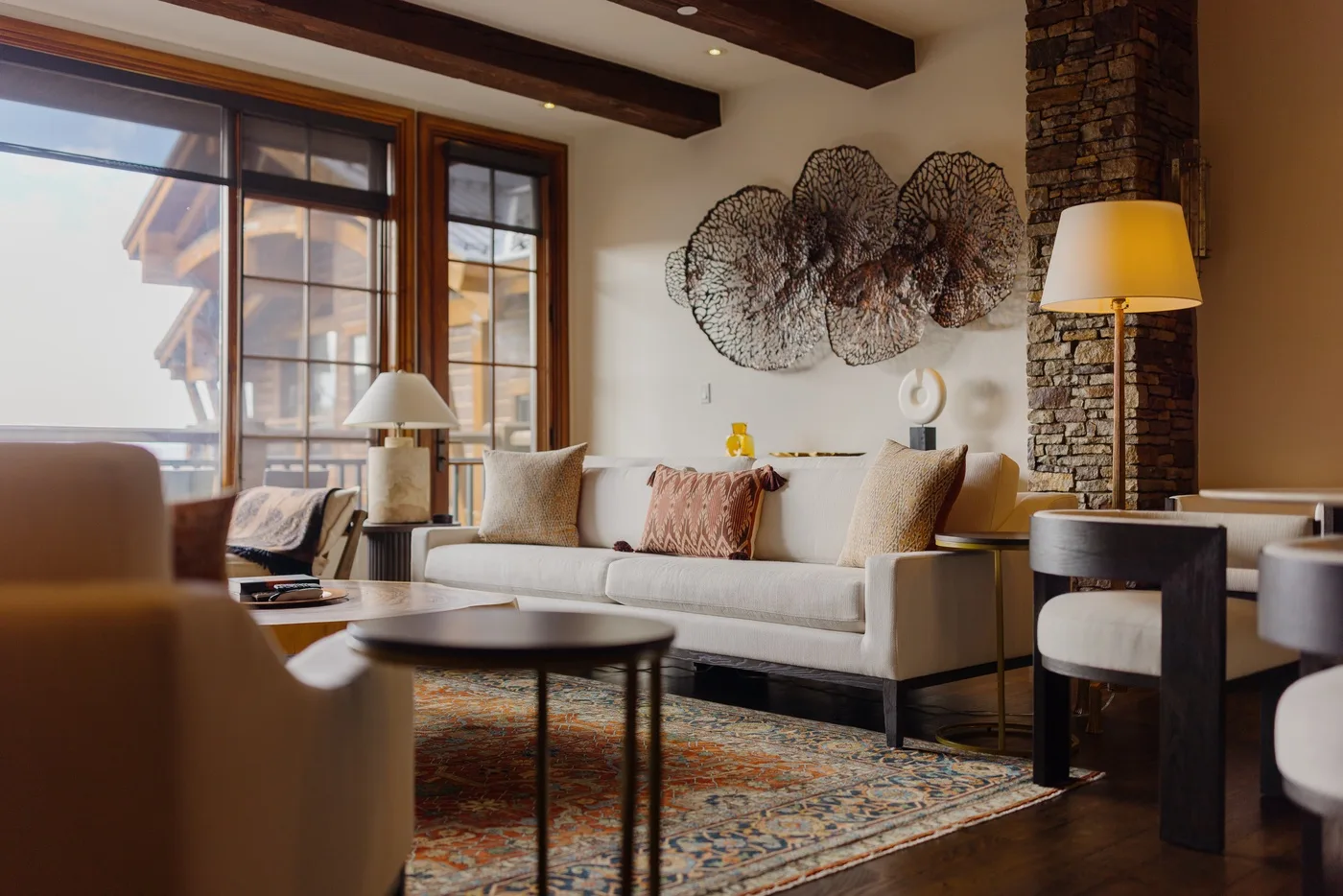 A bright living room with pale seating, large windows, and a patterned rug.