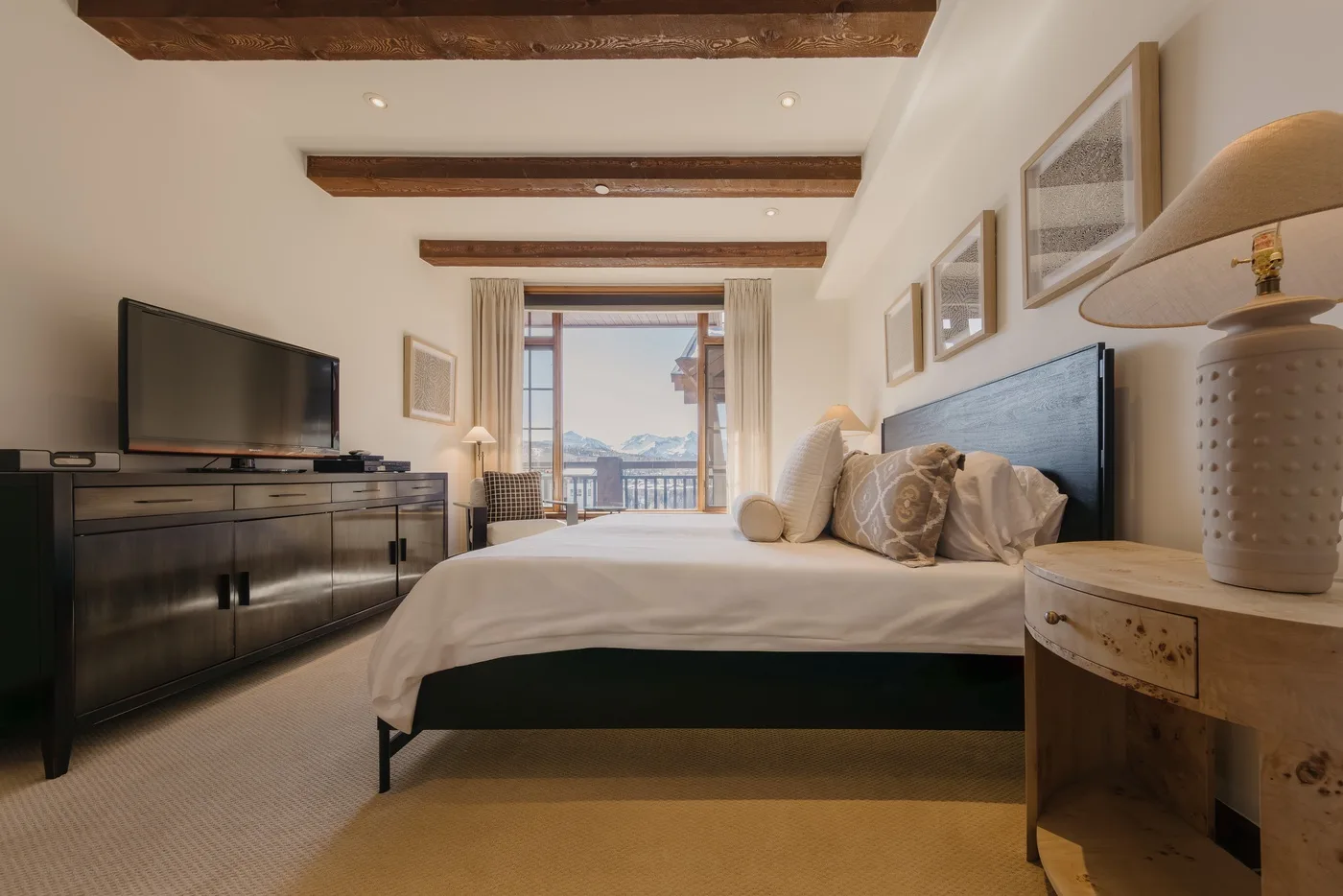 A bedroom with a large bed, dark dresser, and doors opening onto a balcony.