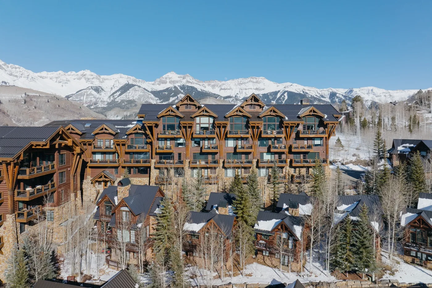 A large lodge-style building stands among snow-covered trees, with mountains in the background.