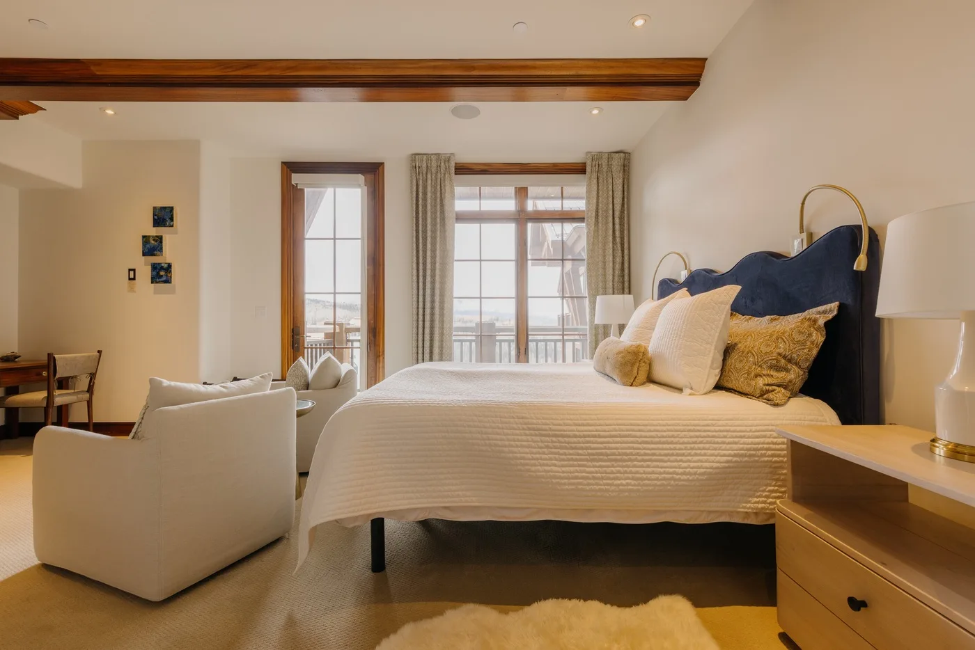 A bedroom with a bed, armchair, and windows with curtains.