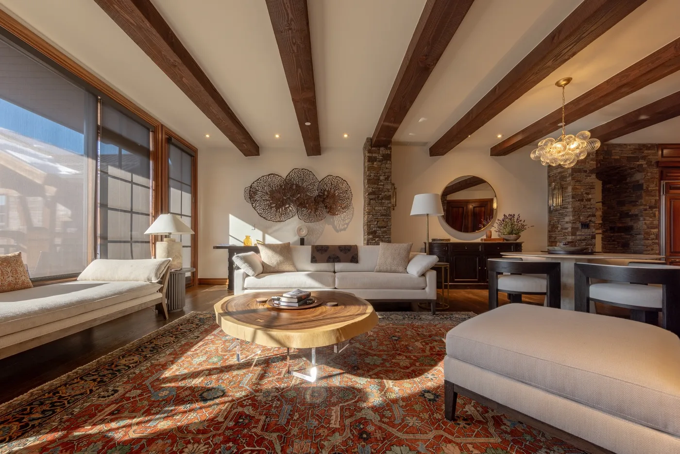 A bright living room with seating, a round coffee table, and exposed ceiling beams.