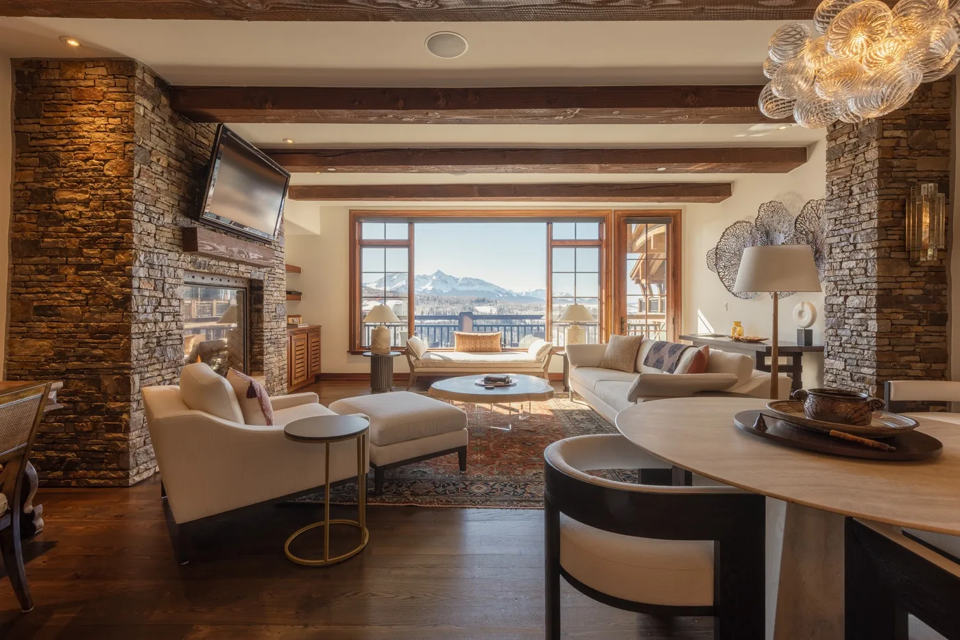 A living room with seating around a coffee table and large windows overlooking the mountains.