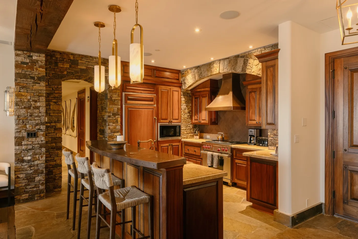 A warm kitchen with wooden cabinetry, a stone wall, and a central island.