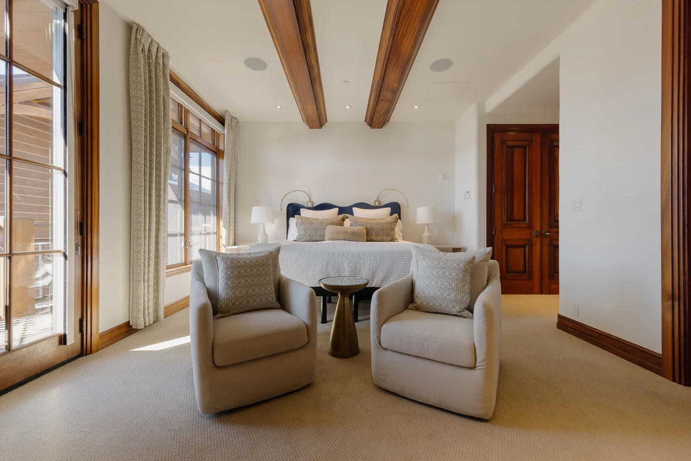A bright bedroom with a bed and two upholstered armchairs.