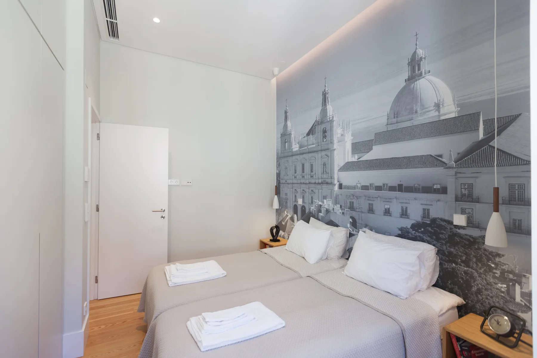 Un dormitorio con dos camas y un gran mural arquitectónico en blanco y negro.