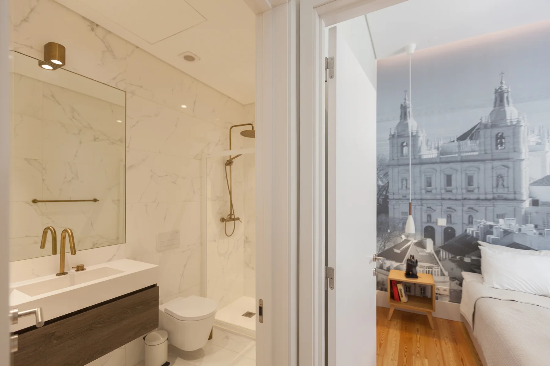 Un baño con lavabo y ducha se abre a un dormitorio con un mural.