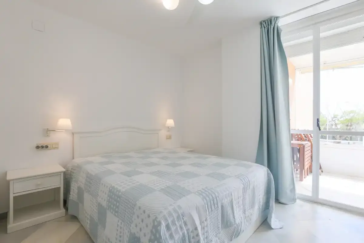 A bedroom with a bed beside a sliding glass door opening onto a balcony.