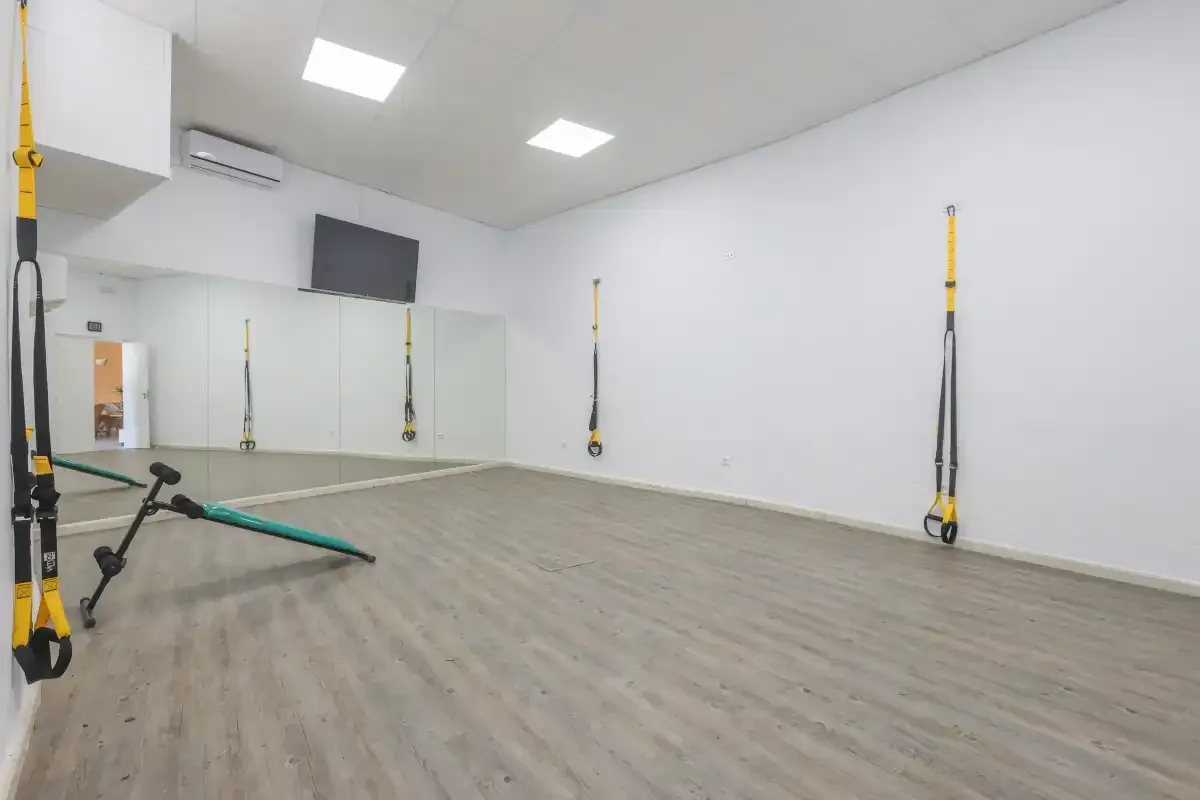 An indoor exercise studio has wall mirrors and suspension straps.