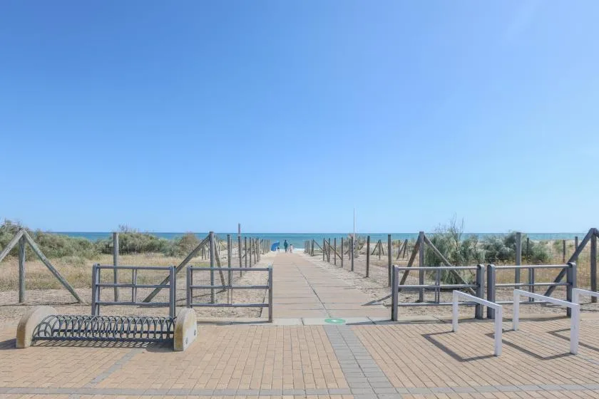 A paved seaside walkway crosses low dune vegetation toward the ocean.