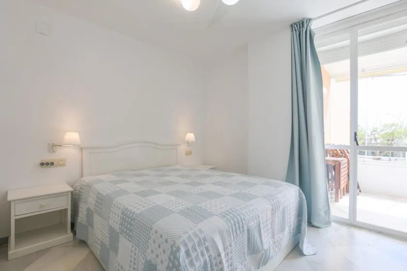 A bright bedroom with a bed beside sliding glass doors opening onto a balcony.
