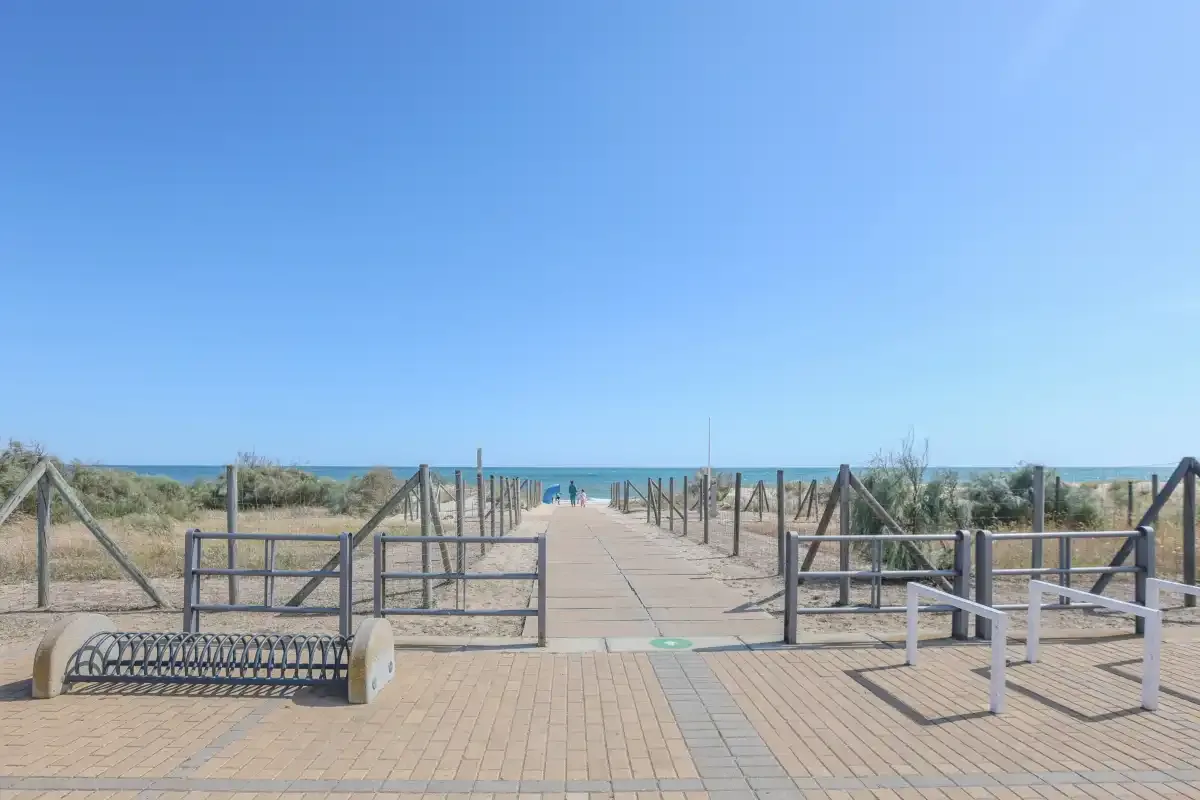 A paved walkway leads across the dunes toward the beach and sea.