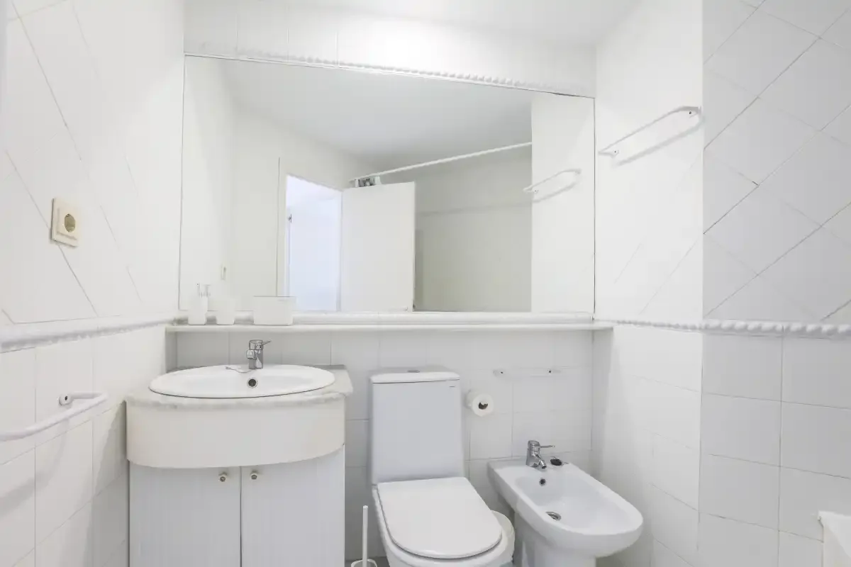 A tiled bathroom with a sink, toilet, bidet, and large wall mirror.