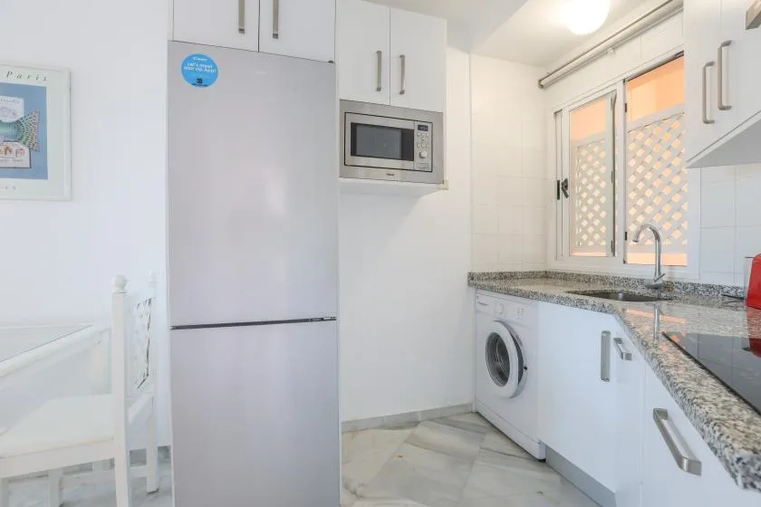 A bright kitchen with white cabinets, a refrigerator, and a washing machine.