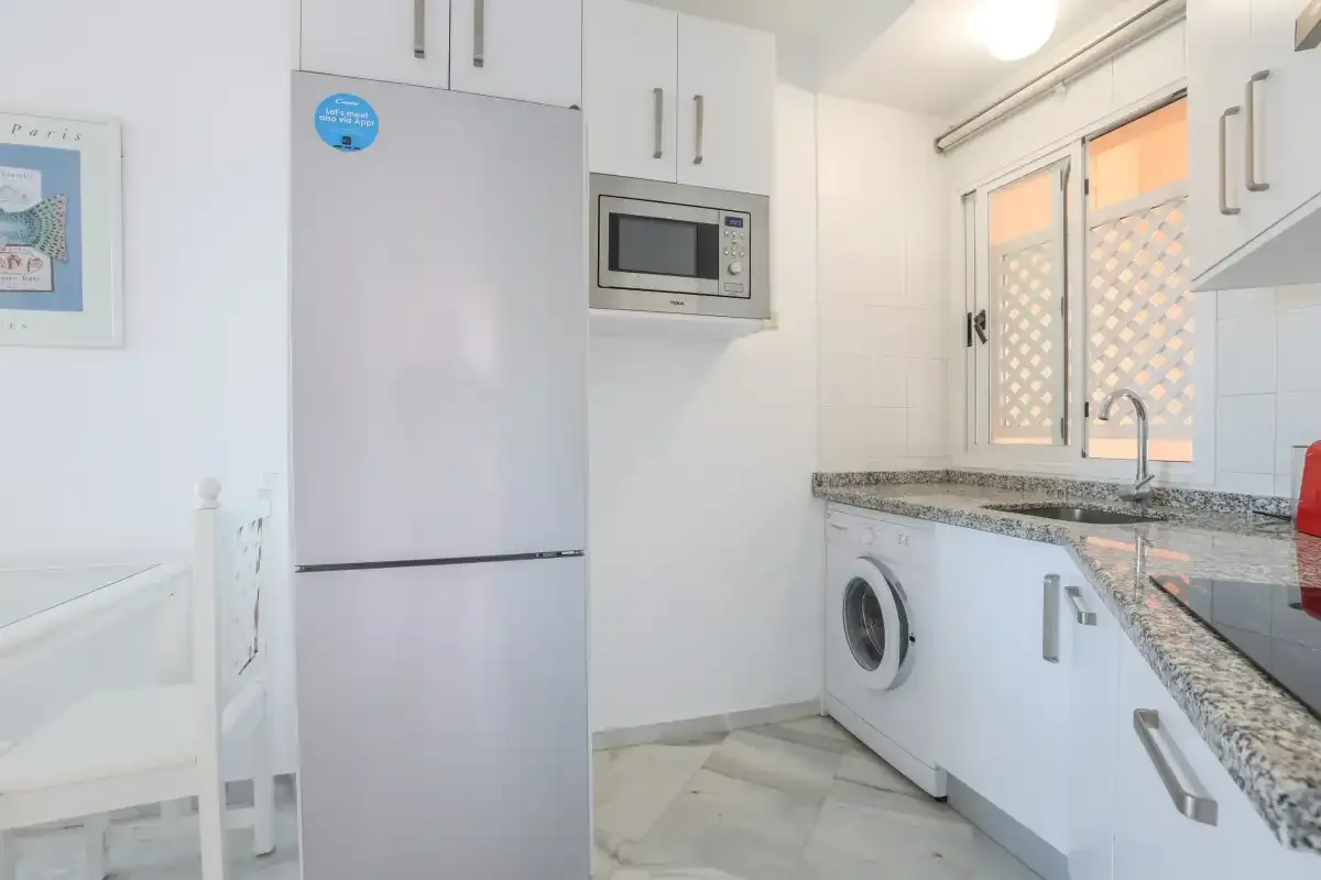 A bright kitchen with white cabinets, a refrigerator, and a countertop.