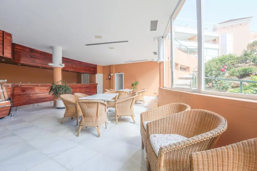 A bright lounge with wicker seating beside large windows overlooking a garden.