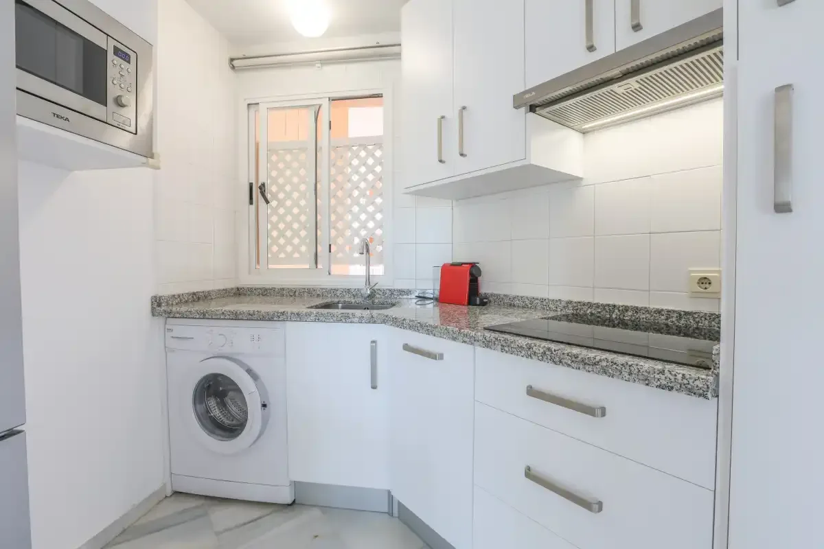 A bright kitchen with white cabinets, a countertop, and a washing machine.
