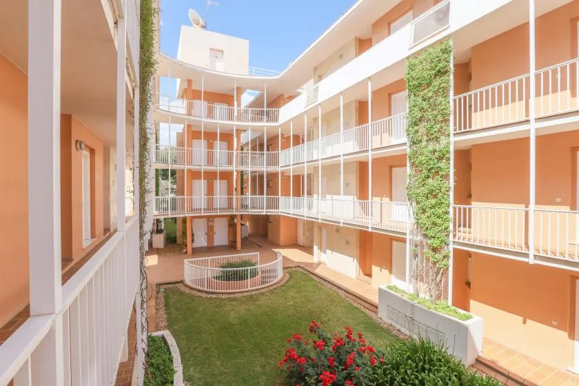 An open courtyard surrounded by orange buildings with balconies and a small garden.