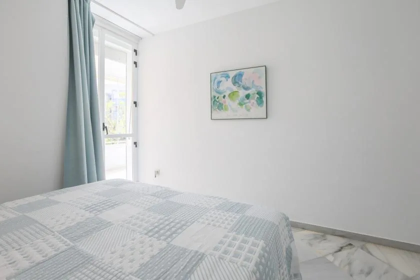 A bedroom with a patterned bedspread, a glass door, and a framed painting.